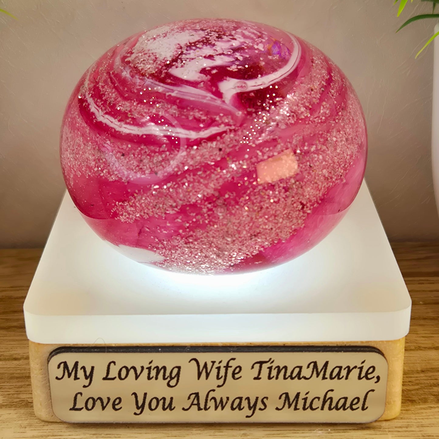 Pink marbled object on a white base with engraved message, placed on a wooden surface.