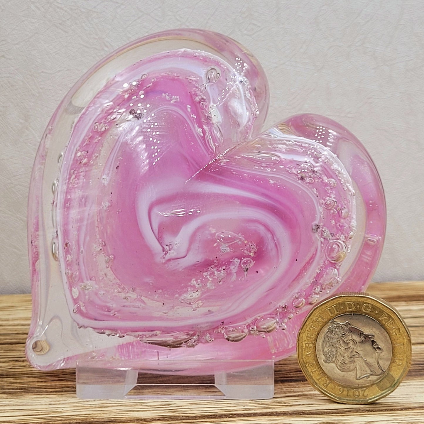 ashes in glass heart in pink next to a one pound coin to demonstrate the size